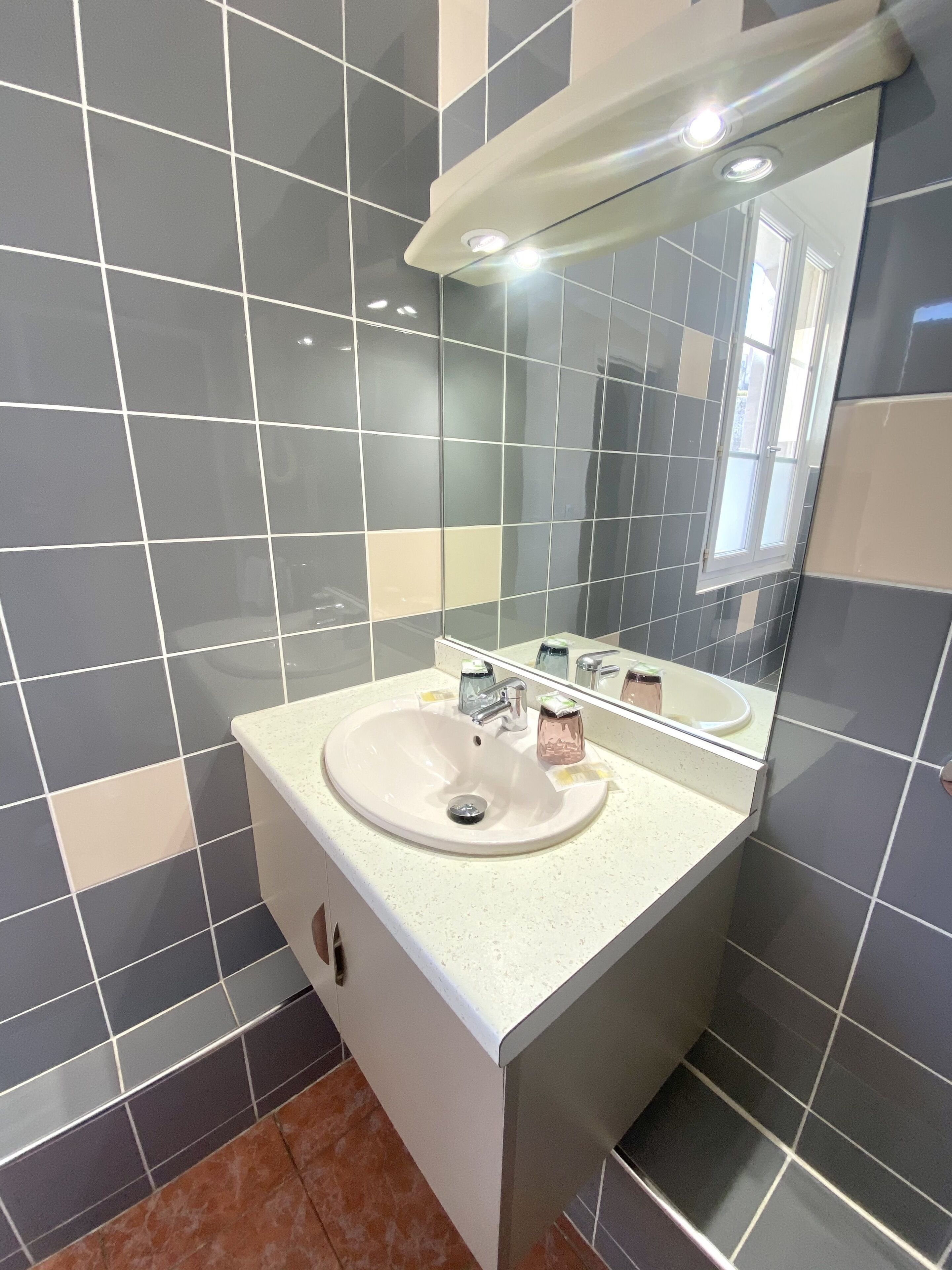 Une salle de bain avec un lavabo blanc, un miroir et des carreaux gris et beige sur les murs.