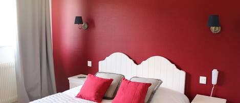 A bedroom with a white headboard, two red pillows, a white bedspread, and a nightstand with a phone.