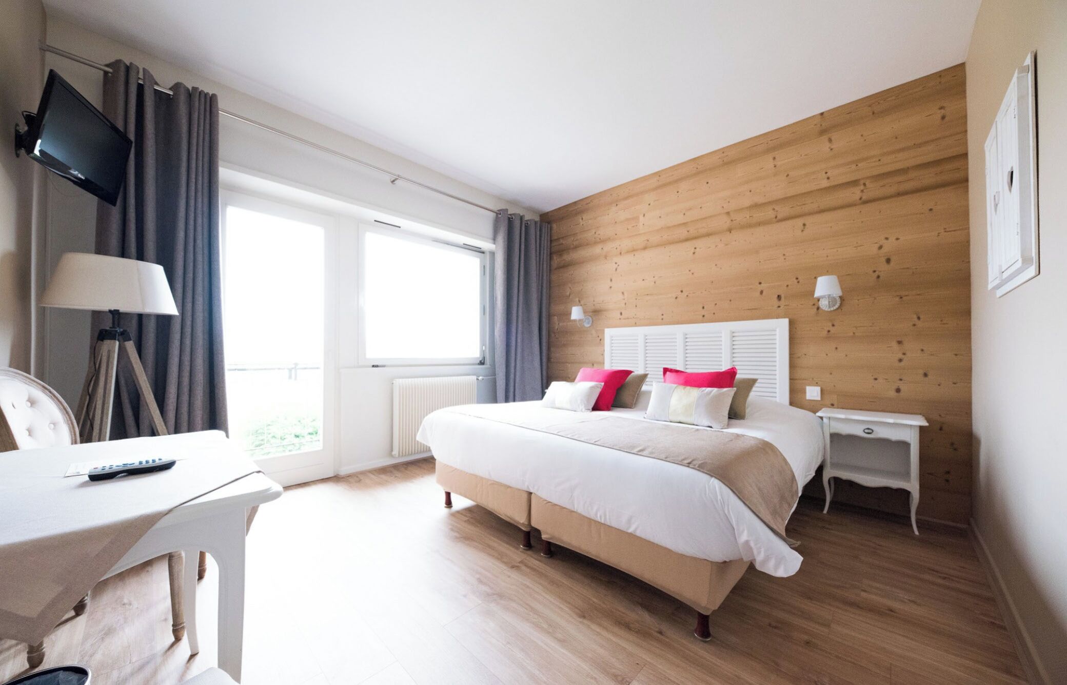 Una habitación de hotel con cama, mesitas de noche, escritorio, televisor y ventana con cortinas.