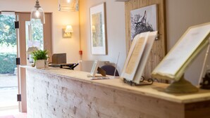 A reception desk with a rustic finish, a potted plant, and framed artwork on the wall. - The Originals Boutique, Hotel Le Kastelberg (Andlau)