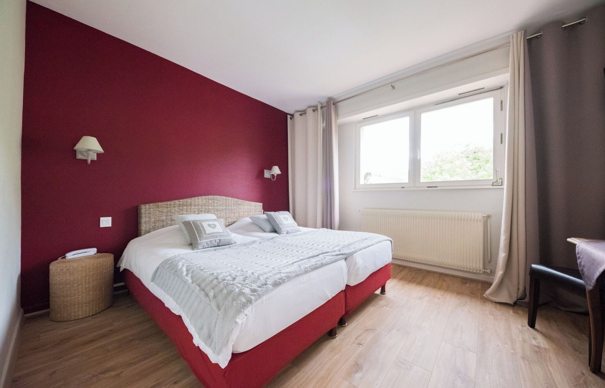 Una cama doble con cabecera roja, una mesita de noche, una lámpara y una ventana con cortinas.