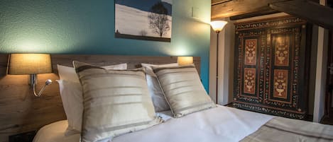 Een slaapkamer met een bed, kussens, een nachtkastje, een wandlamp en een decor kast.