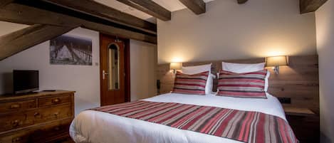 Een slaapkamer met een groot bed, houten balken, een dressoir en een televisie op een dressoir.