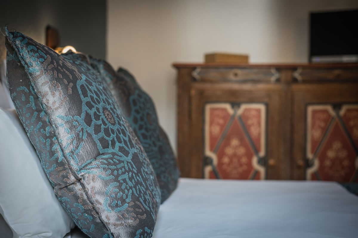 Un llit amb almoadins estampats i un armari de fusta amb panells decoratius.