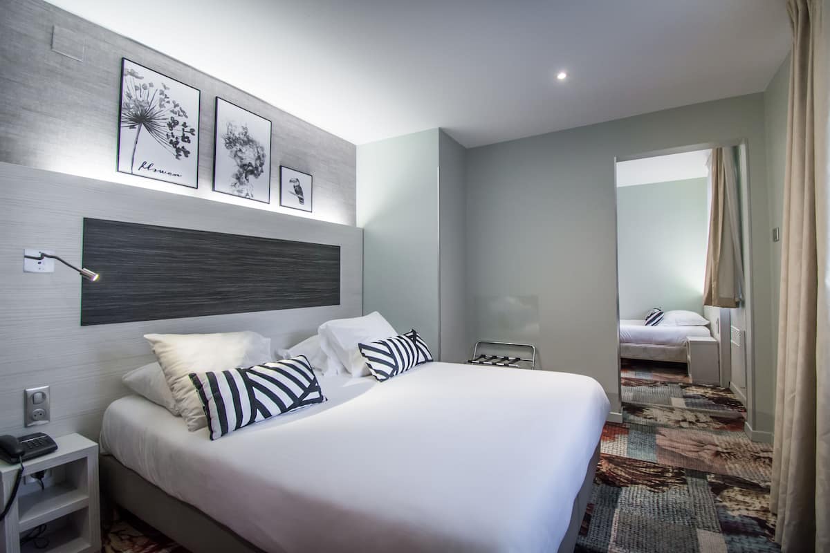 A modern hotel room with a large bed, a bedside table, a nightstand, and a headboard. There are two framed pictures on the wall above the bed.