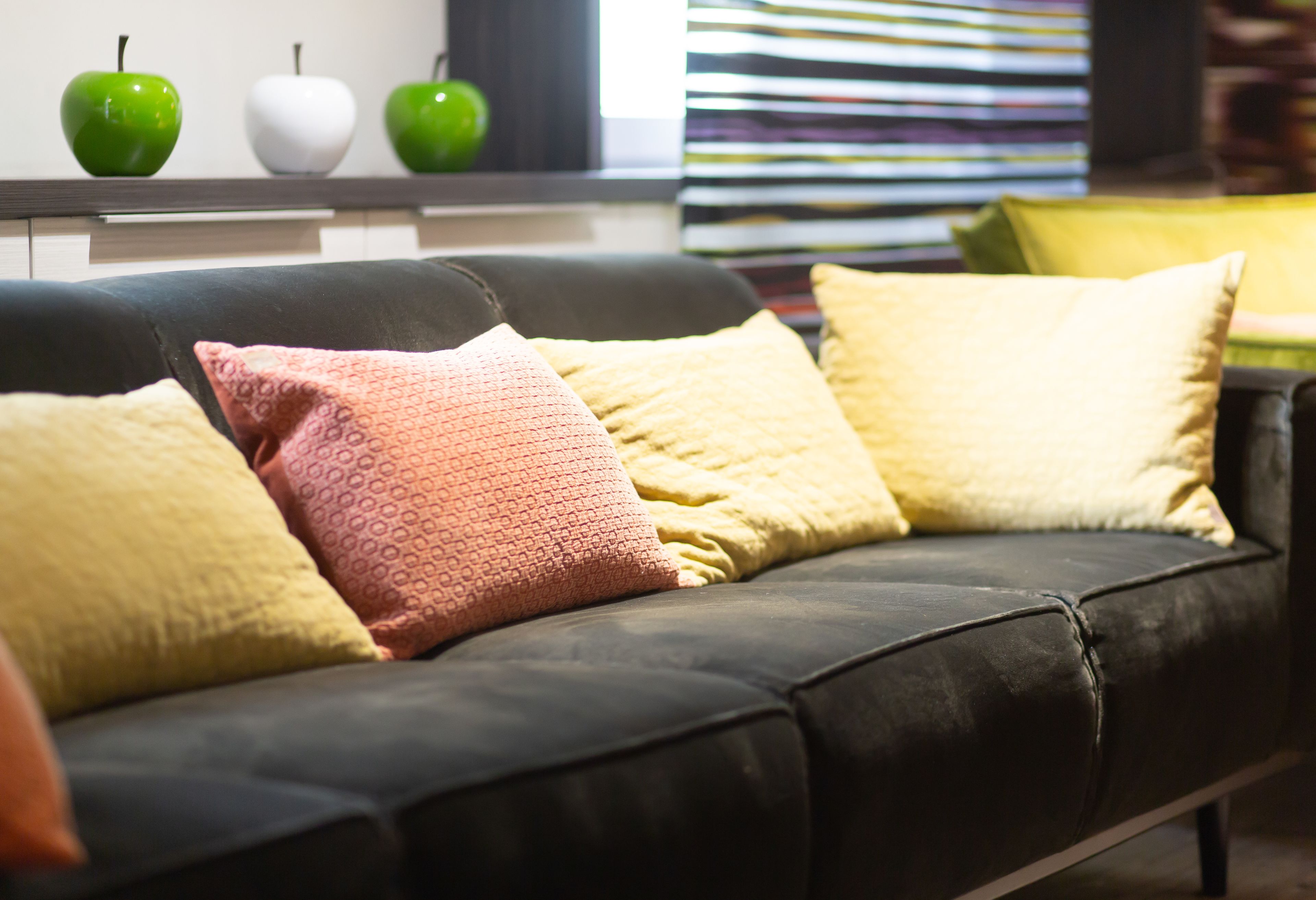 Un sofá de cuero negro con tres almohadones en amarillo, rosa y blanco.