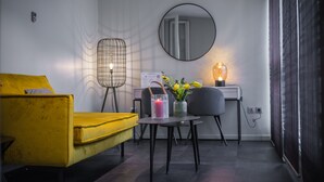 A modern living room with a yellow sofa, a round mirror, a small table with a vase of flowers, and a lamp. - Couvent du Franciscain (Strasbourg)