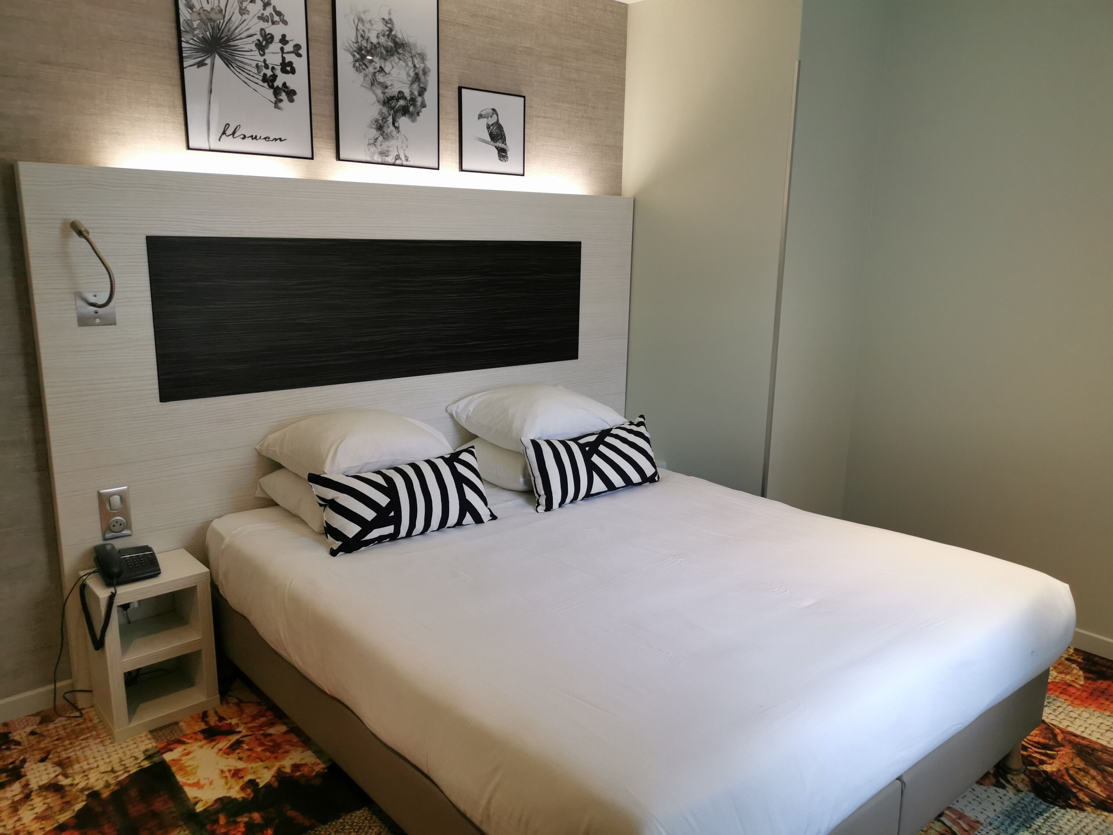 A neatly made bed with white bedding and striped pillows, a bedside table with a phone, and artwork on the wall.