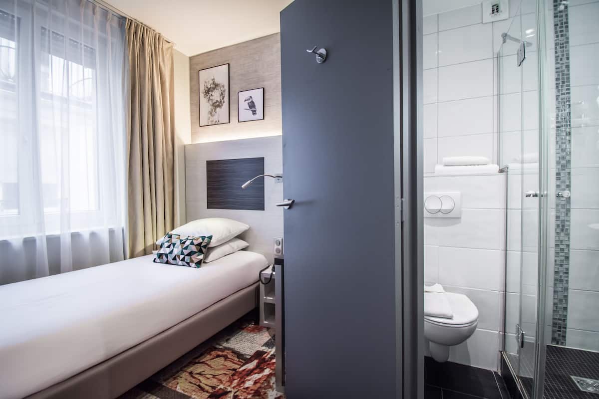 A hotel room with a bed, a bedside table, a nightstand, a shower area, and a toilet.