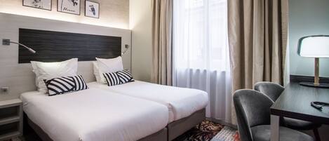 A hotel room with two beds, a desk, and a chair. There are three framed pictures on the wall above the beds.