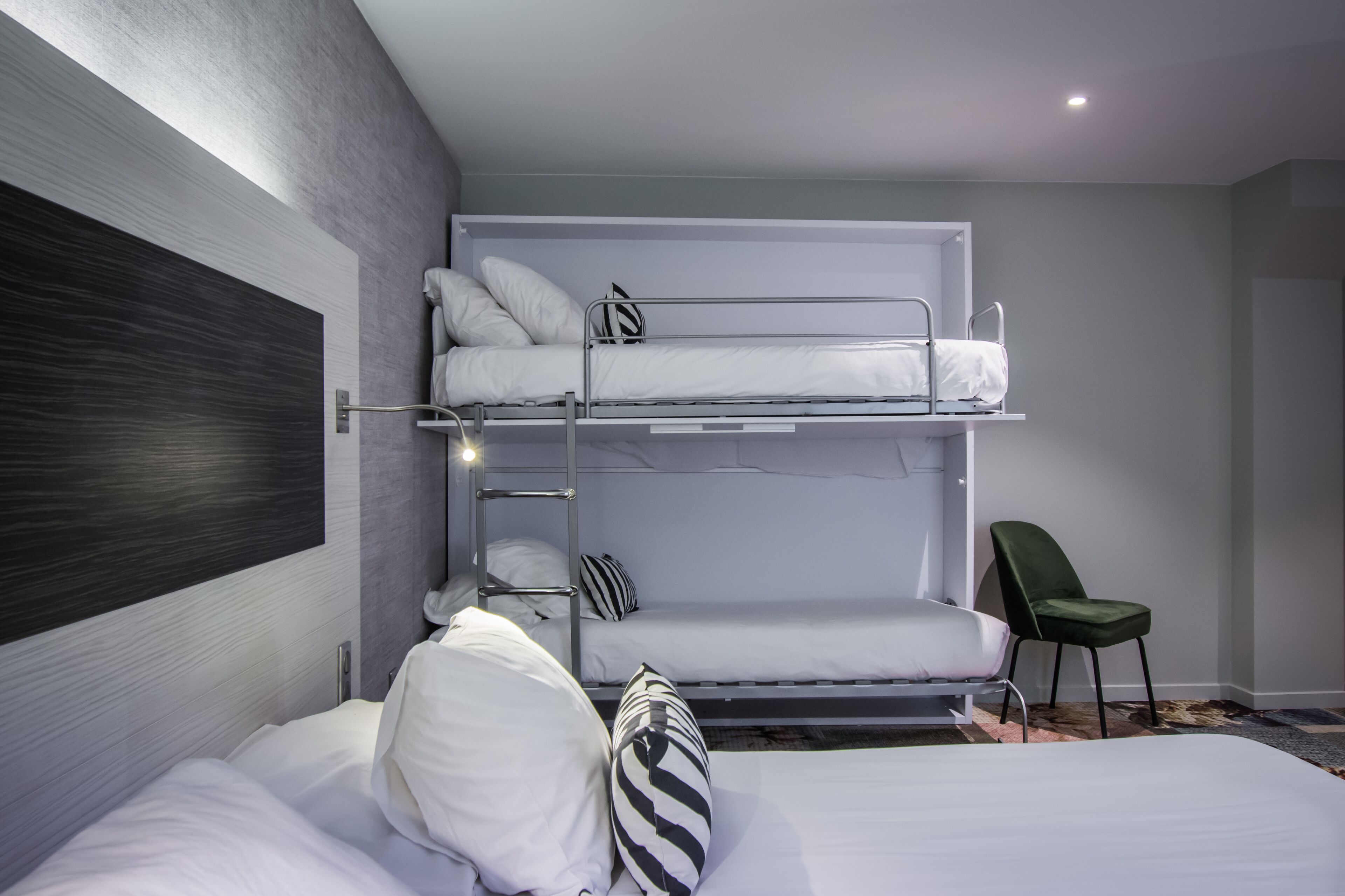 A bunk bed room with a headboard, a green chair, and a patterned rug.