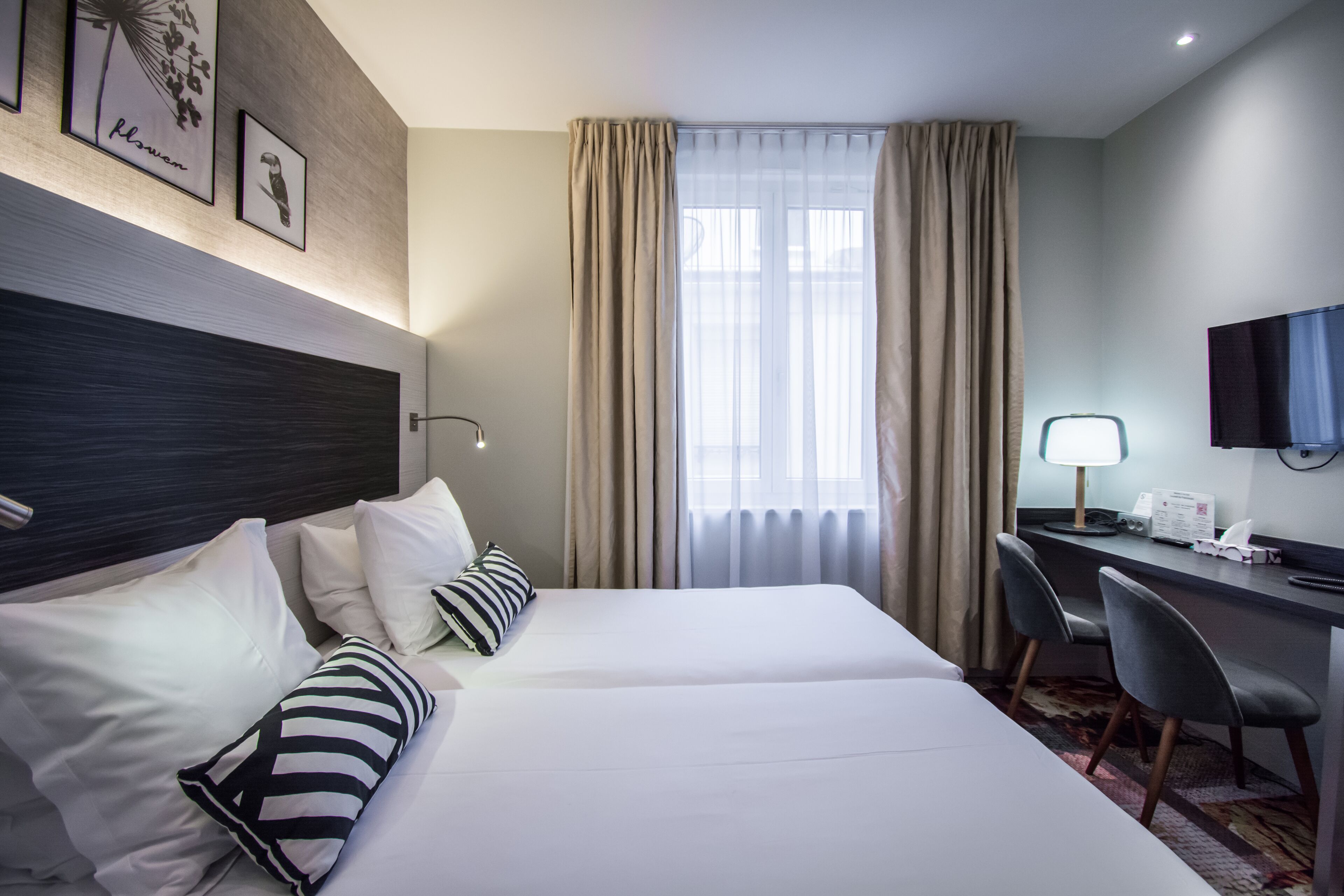 A hotel room with a bed, a desk, a chair, a TV, and curtains.