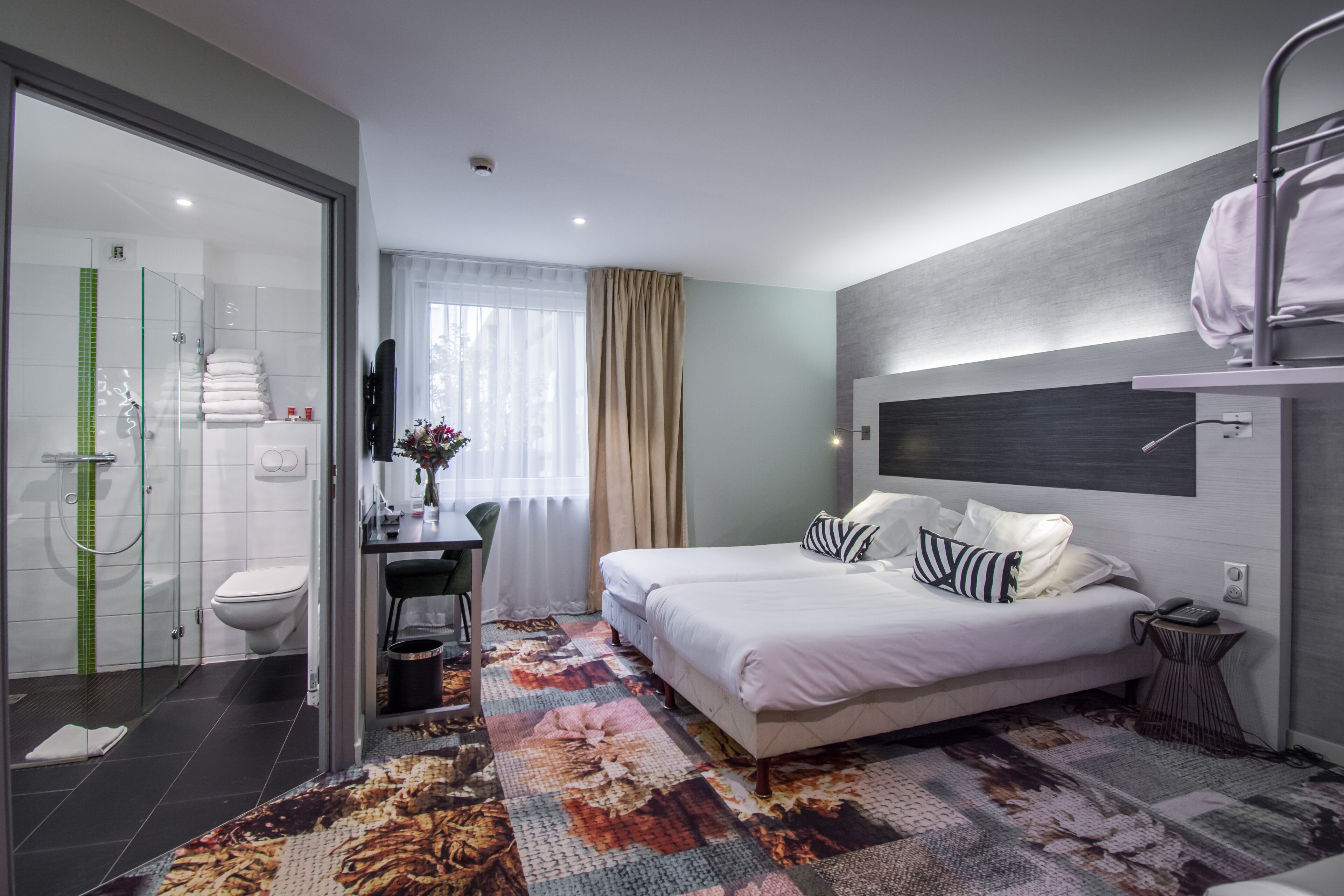 A modern hotel room with a large bed, a desk, a shower area, and a view of the outdoors.