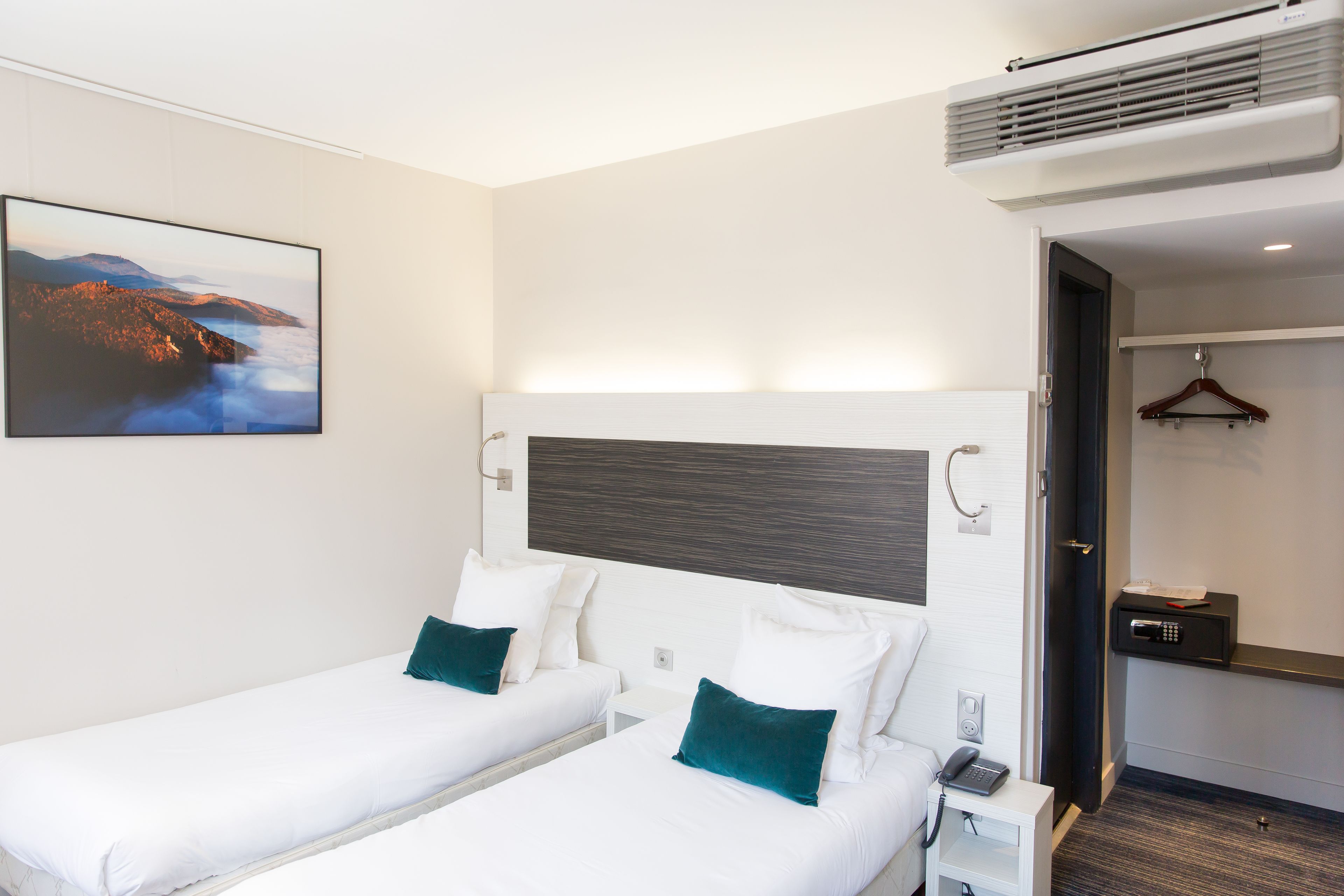 A hotel room with two beds, a painting on the wall, a bedside table with a phone, and a door leading to a bathroom.