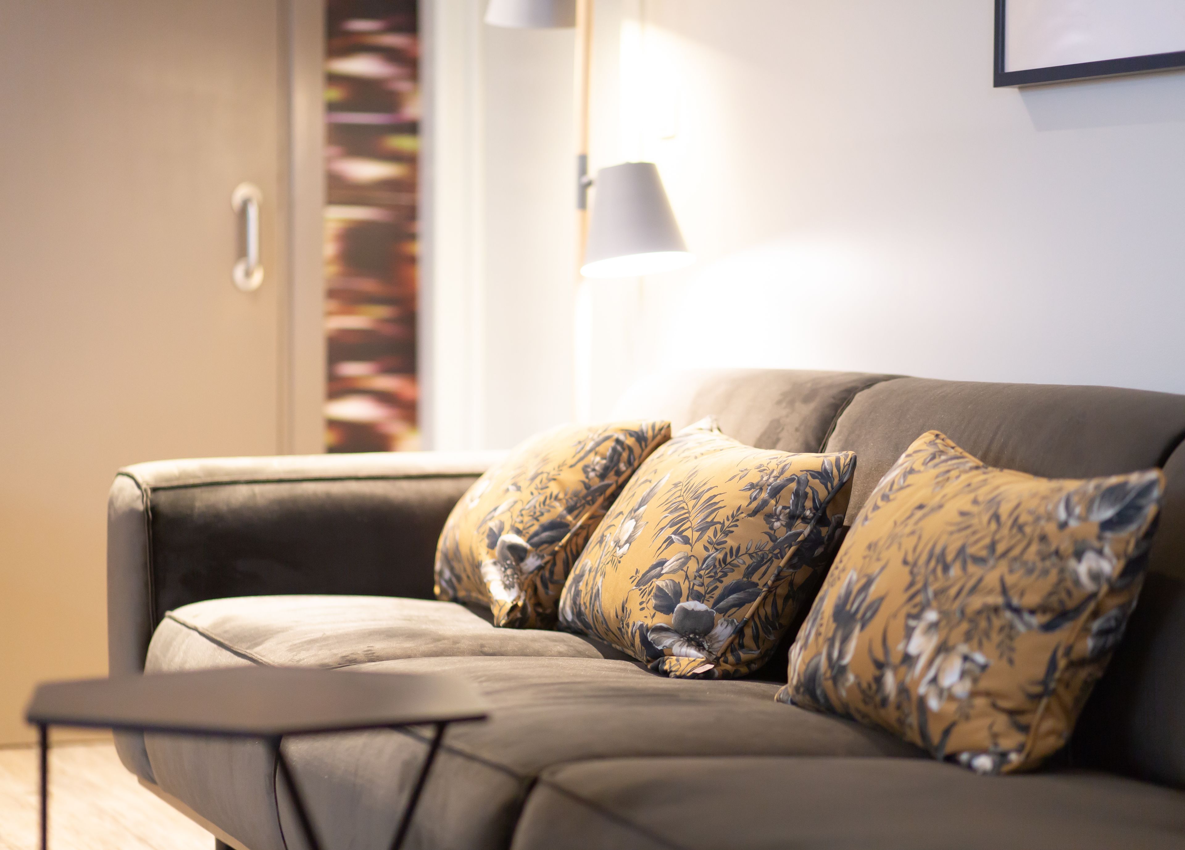 A modern living room with a sofa and matching cushions, a side table, and a lamp.