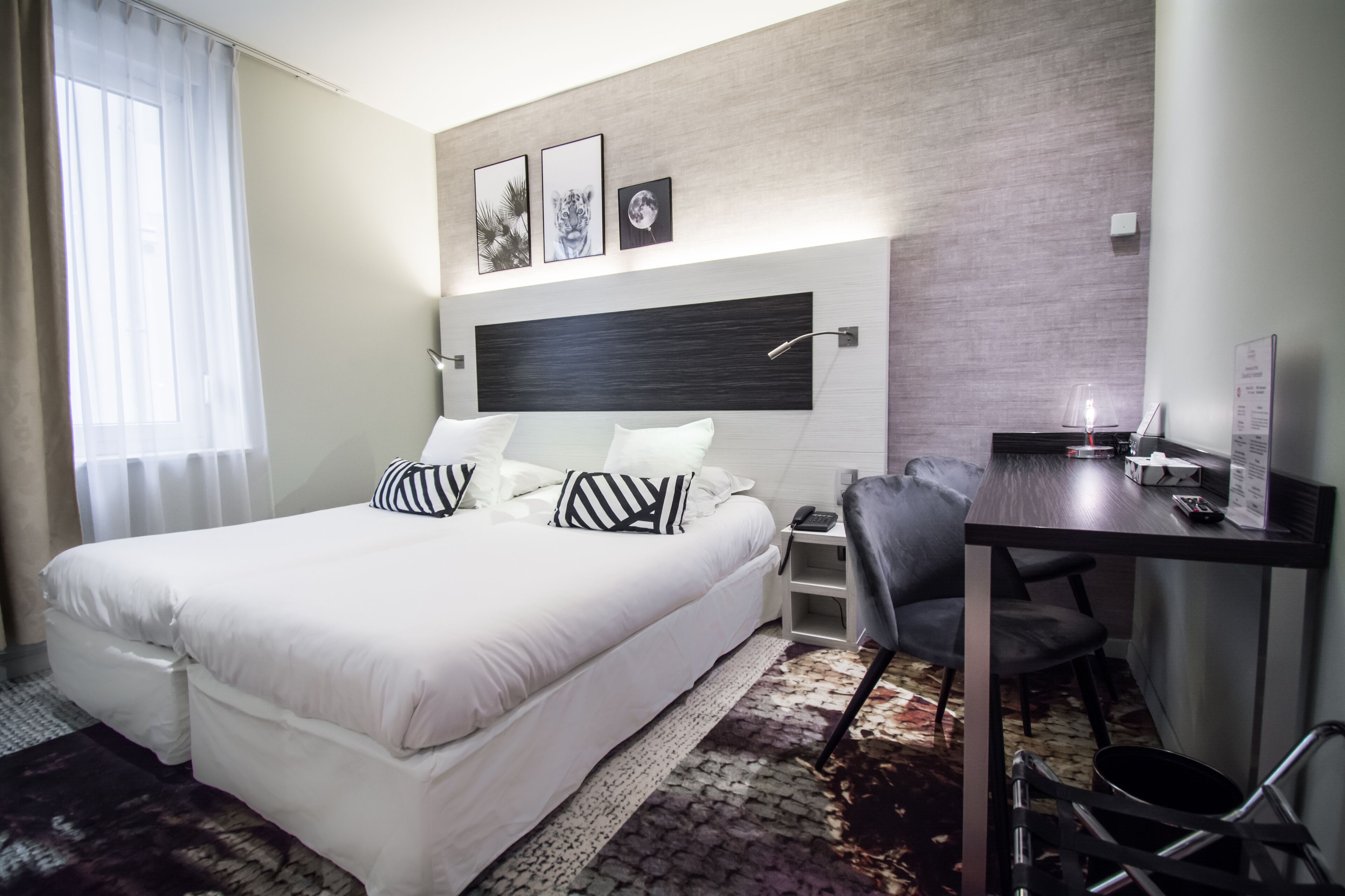 A hotel room with a large bed, a desk, and a chair. There are three framed pictures on the wall above the bed.