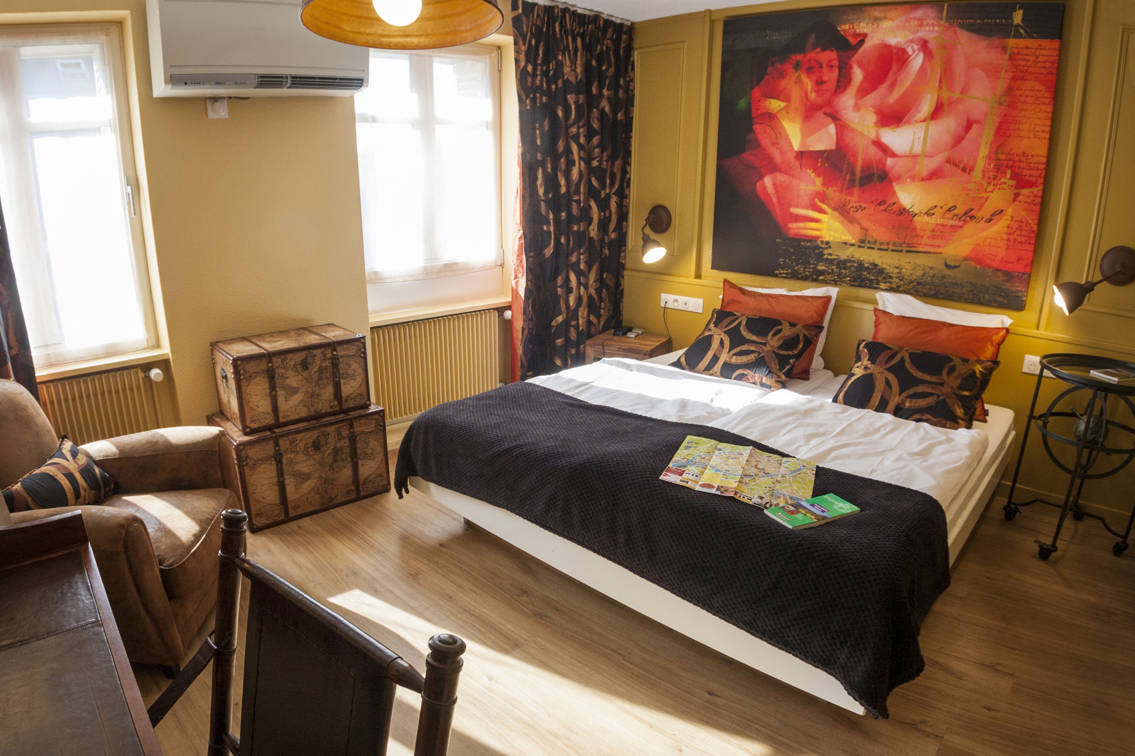 A bedroom with a large bed, a chest of drawers, a chair, a table, and a poster on the wall.