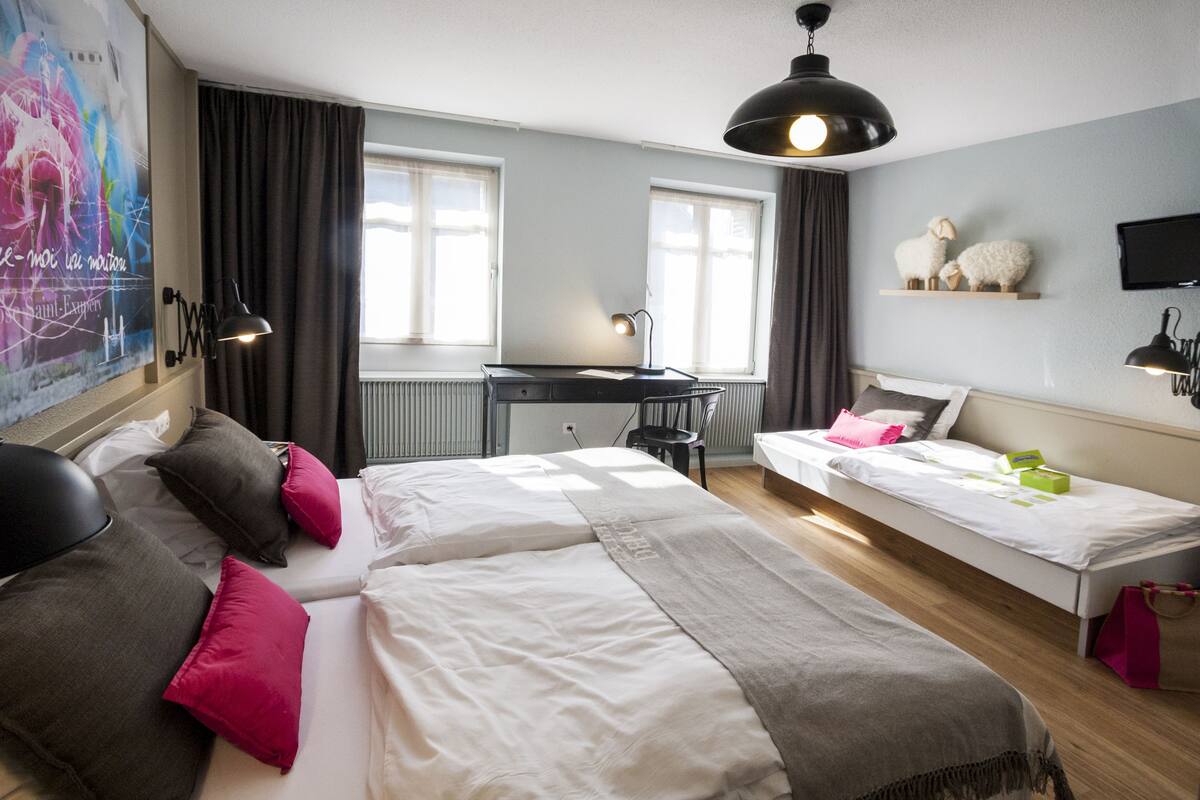A modern hotel room with a large bed, a smaller bed, a desk, and a TV.