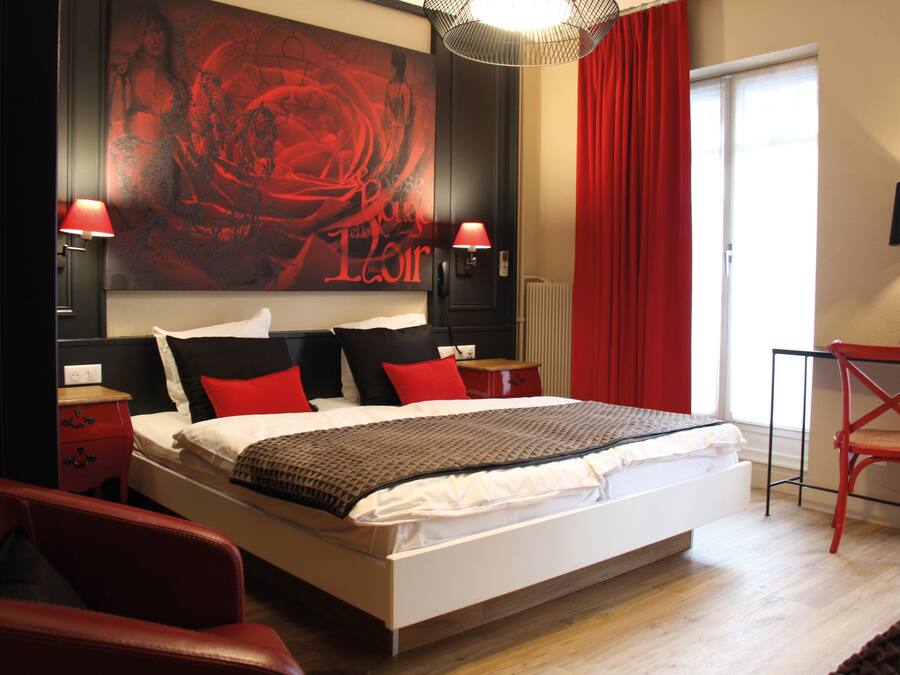Un dormitorio moderno con una cama grande, decoración en rojo y negro, y una silla roja.