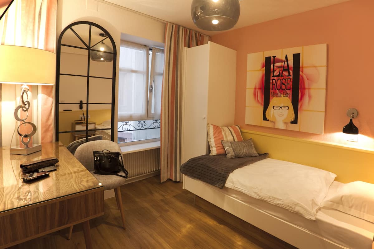 A bedroom with a bed, a desk with a chair, a mirror, a window with curtains, and a wall with a poster.