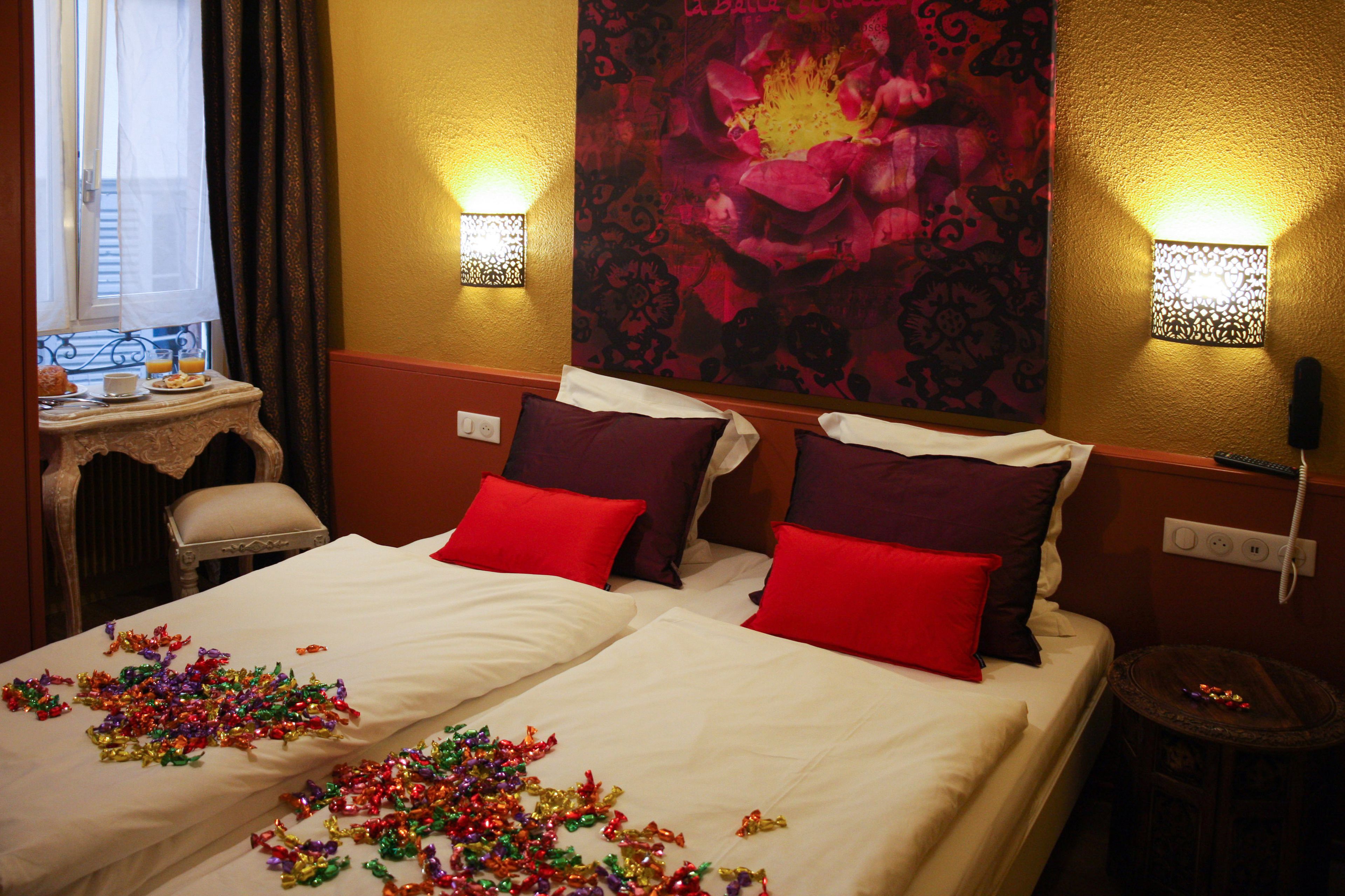 A hotel room with two beds, red and white pillows, decorative tinsel, and a large floral tapestry on the wall.