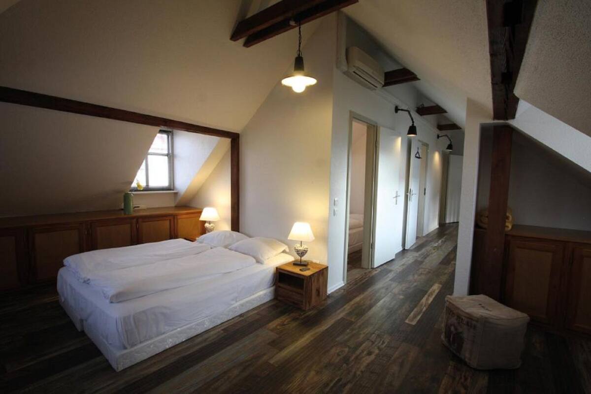 A bedroom with a large bed, wooden flooring, and a sloped ceiling with exposed beams.