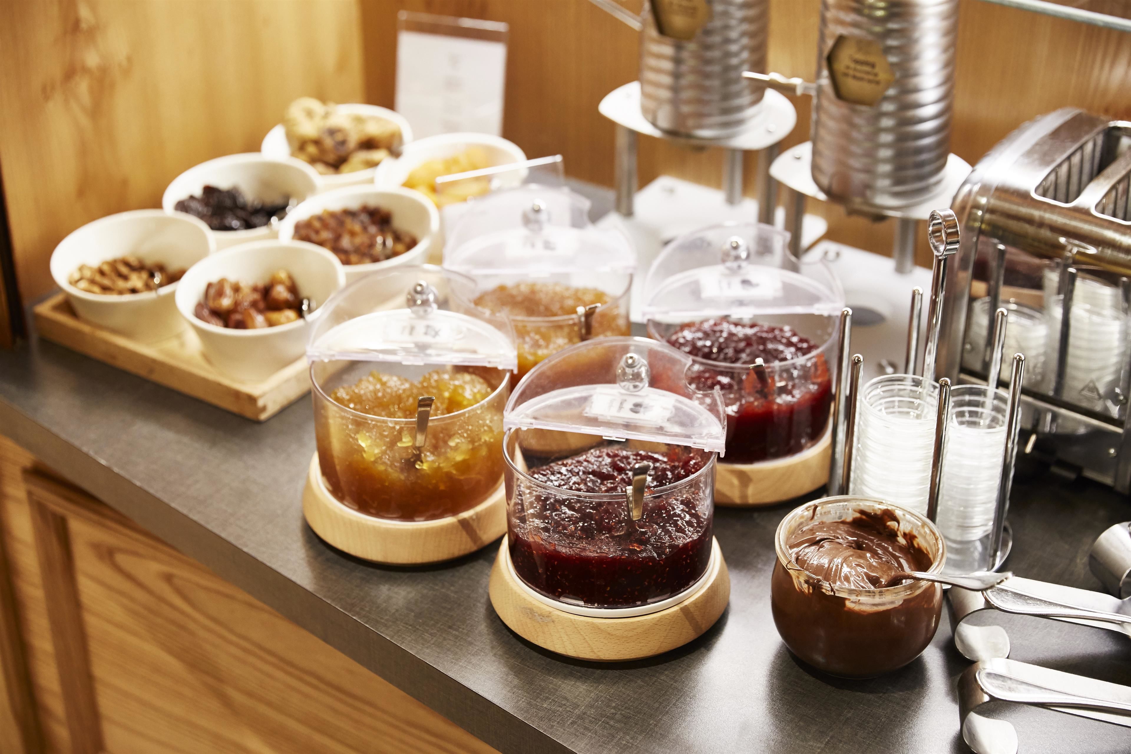 Un bufé con diversos alimentos en recipientes transparentes, incluyendo mermeladas y pastas.