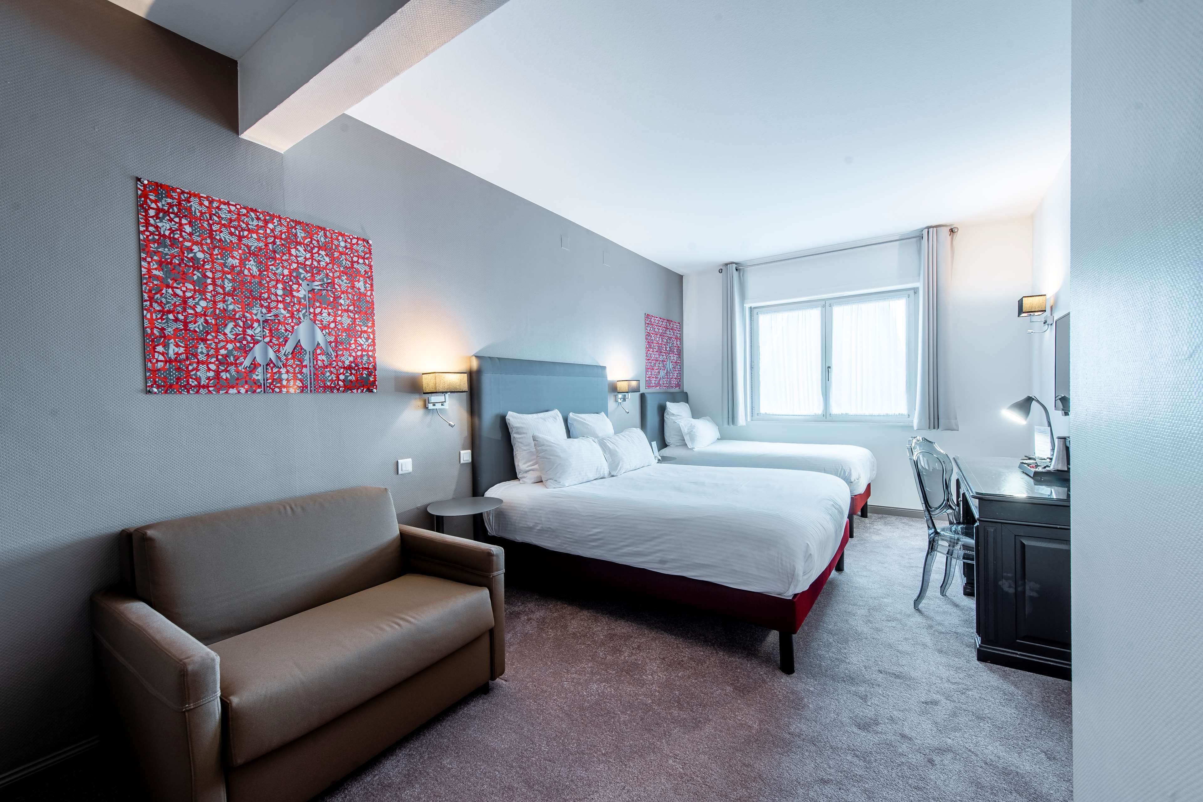 A hotel room with a large bed, a sofa, a desk, and artwork on the walls.