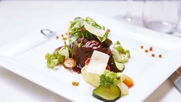A white plate with a steak topped with greens, cheese, and vegetables.