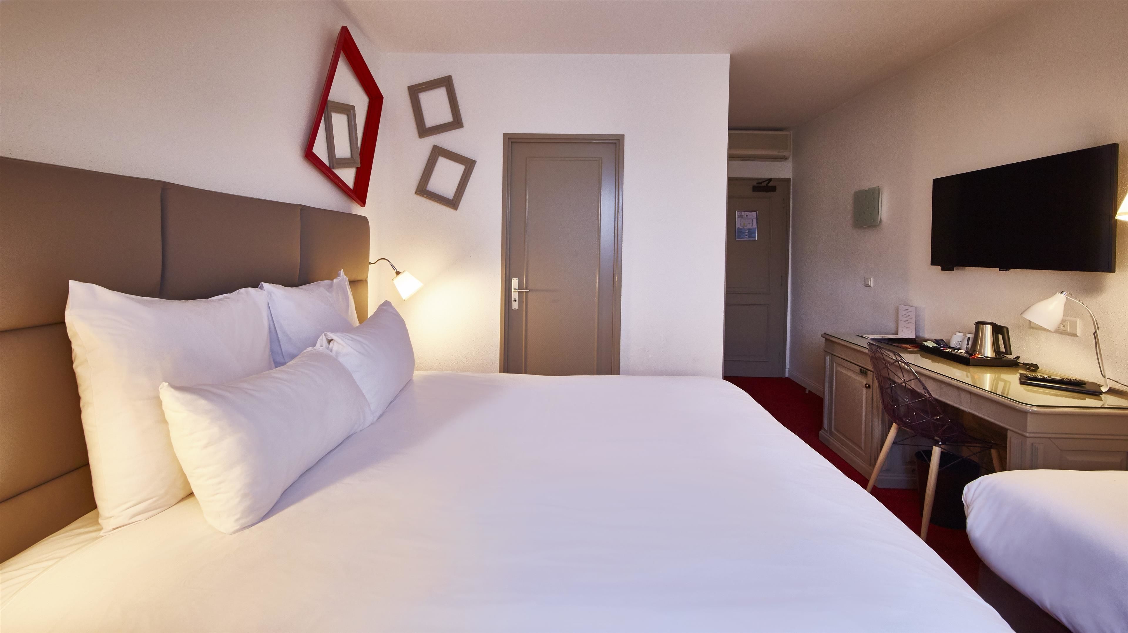 A hotel room with a large bed, a desk, a chair, a television, and a door.