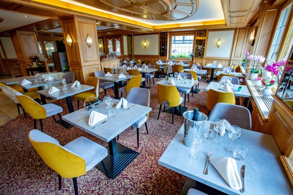 A restaurant with multiple tables, chairs, and a patterned carpet.