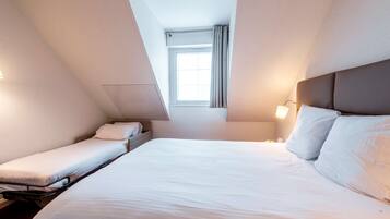Una habitación de hotel con una cama grande, una cama más pequeña, una ventana y una mesita de noche con lámpara.