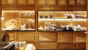 A well-lit breakfast bar with wooden cabinets, a coffee machine, and a variety of breakfast items. - Best Western Plus Au Cheval Blanc Mulhouse Nord (Baldersheim)