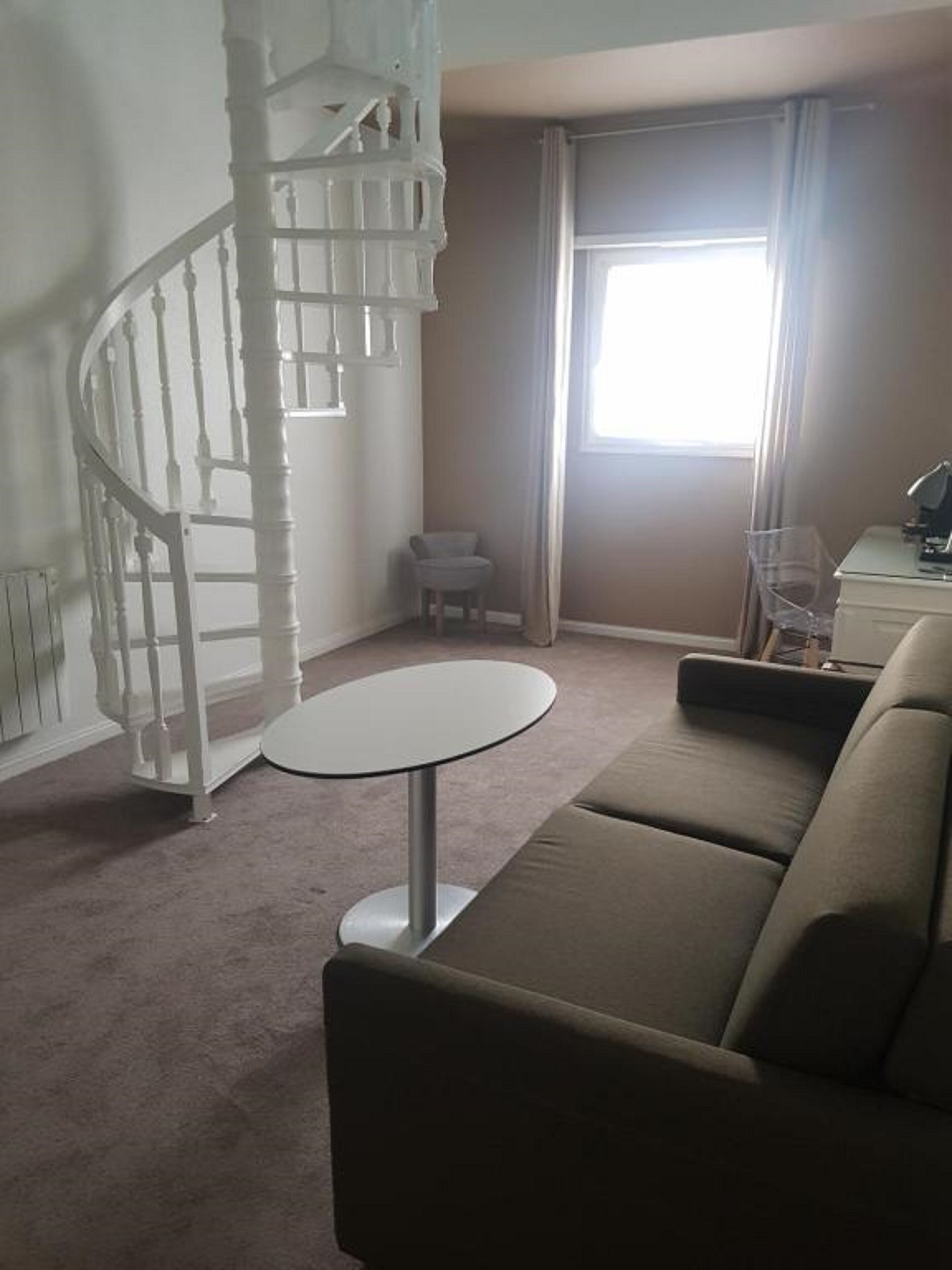 Una sala de estar con una escalera espiral, una mesa redonda, un sofá y un ventanal con cortinas.
