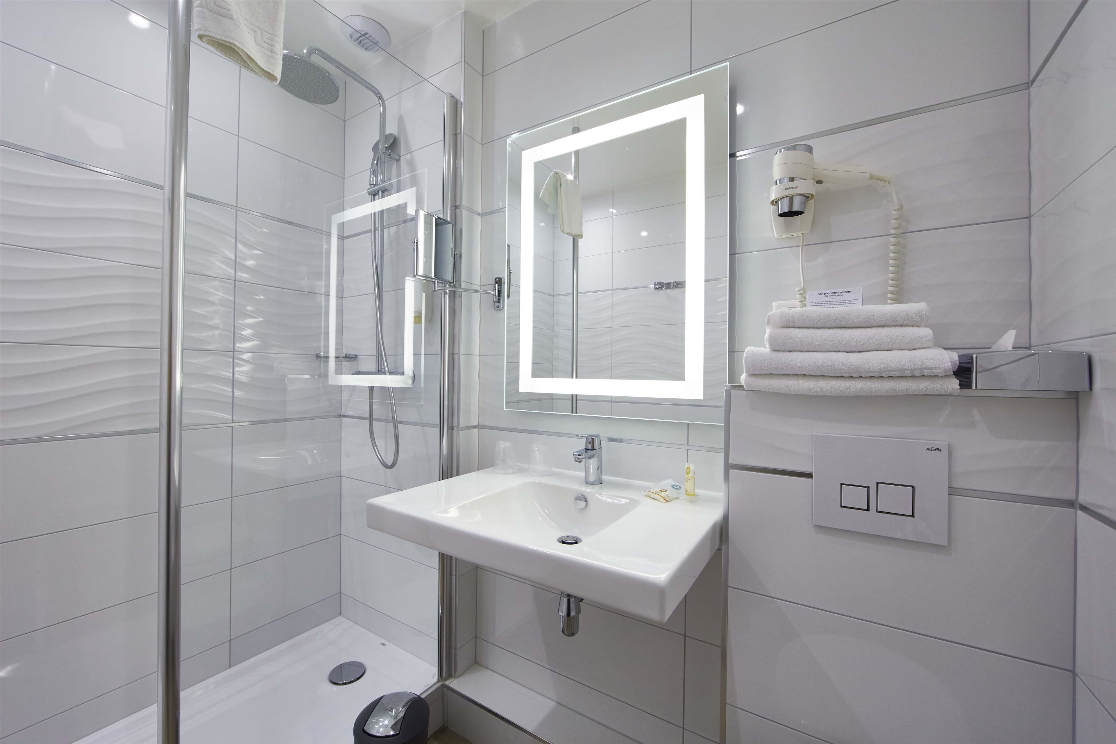 Un baño moderno con ducha de vidrio, lavabo blanco e iluminación integrada en el espejo.