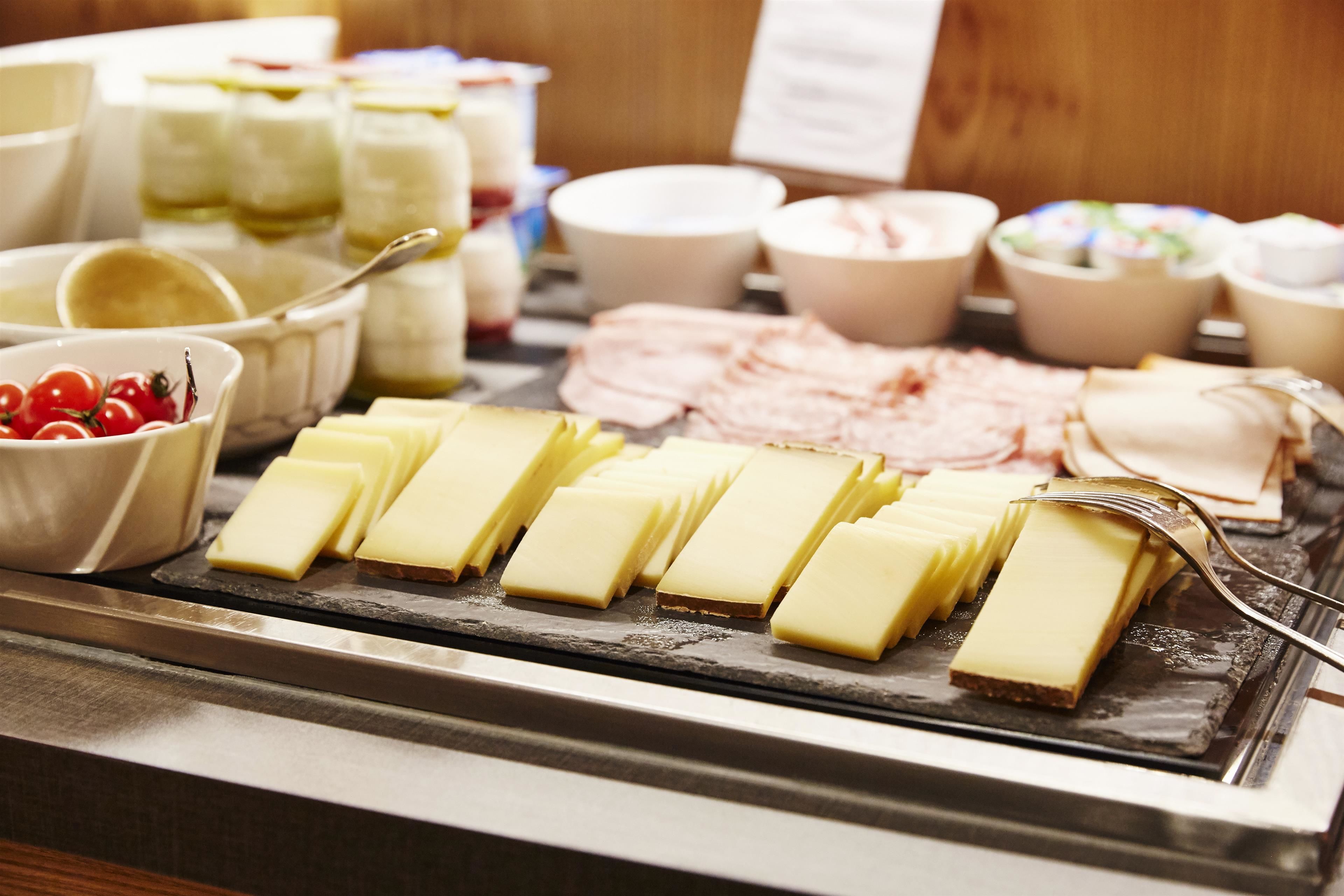 Een buffet met diverse soorten eten, waaronder kaas, ham en kersen-tomaten.