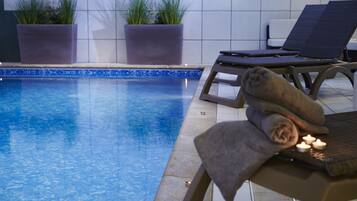Un área junto a la piscina con sillones de descanso, una mesa con toallas y velas, y plantas en macetas.