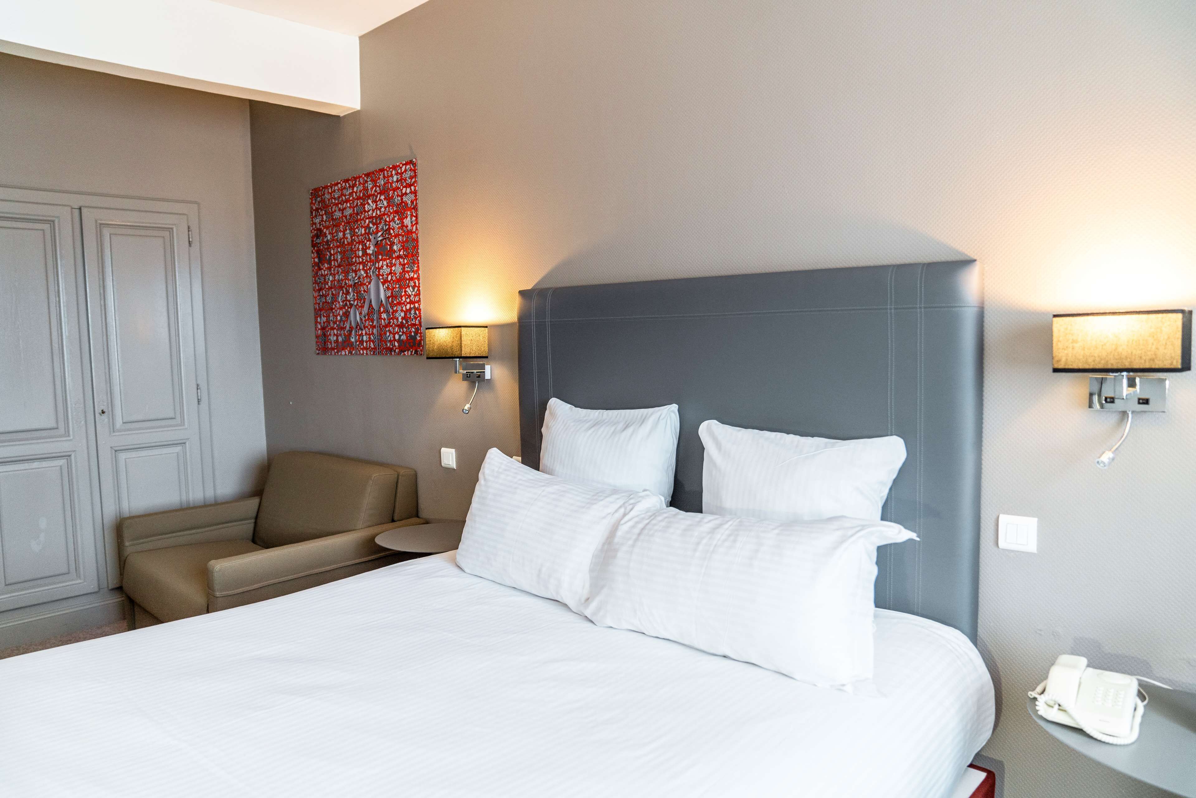 A hotel room with a large bed, a sofa, two wall-mounted lamps, and a telephone on the nightstand.