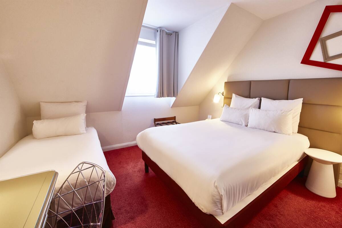 A hotel room with a large bed, a smaller bed, a desk, and a chair. There are two bedside tables with lamps.