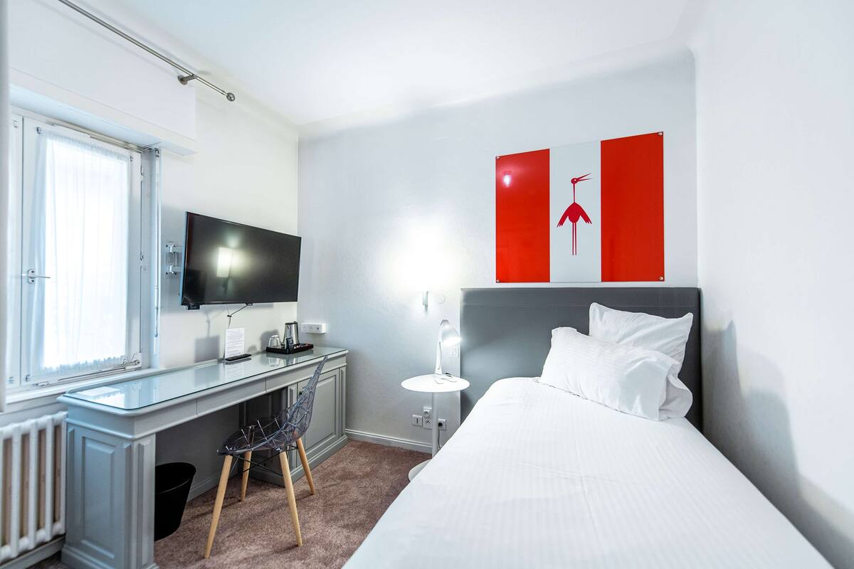 A hotel room with a bed, a desk with a computer, a TV, and a wall-mounted light.