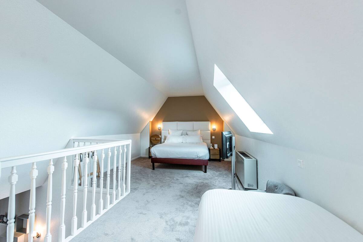 A bedroom with a sloped ceiling, a bed, a TV, and a small table.