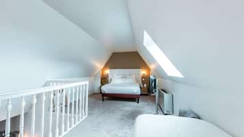 Un dormitorio con techo inclinado, una cama, un televisor y una mesita.