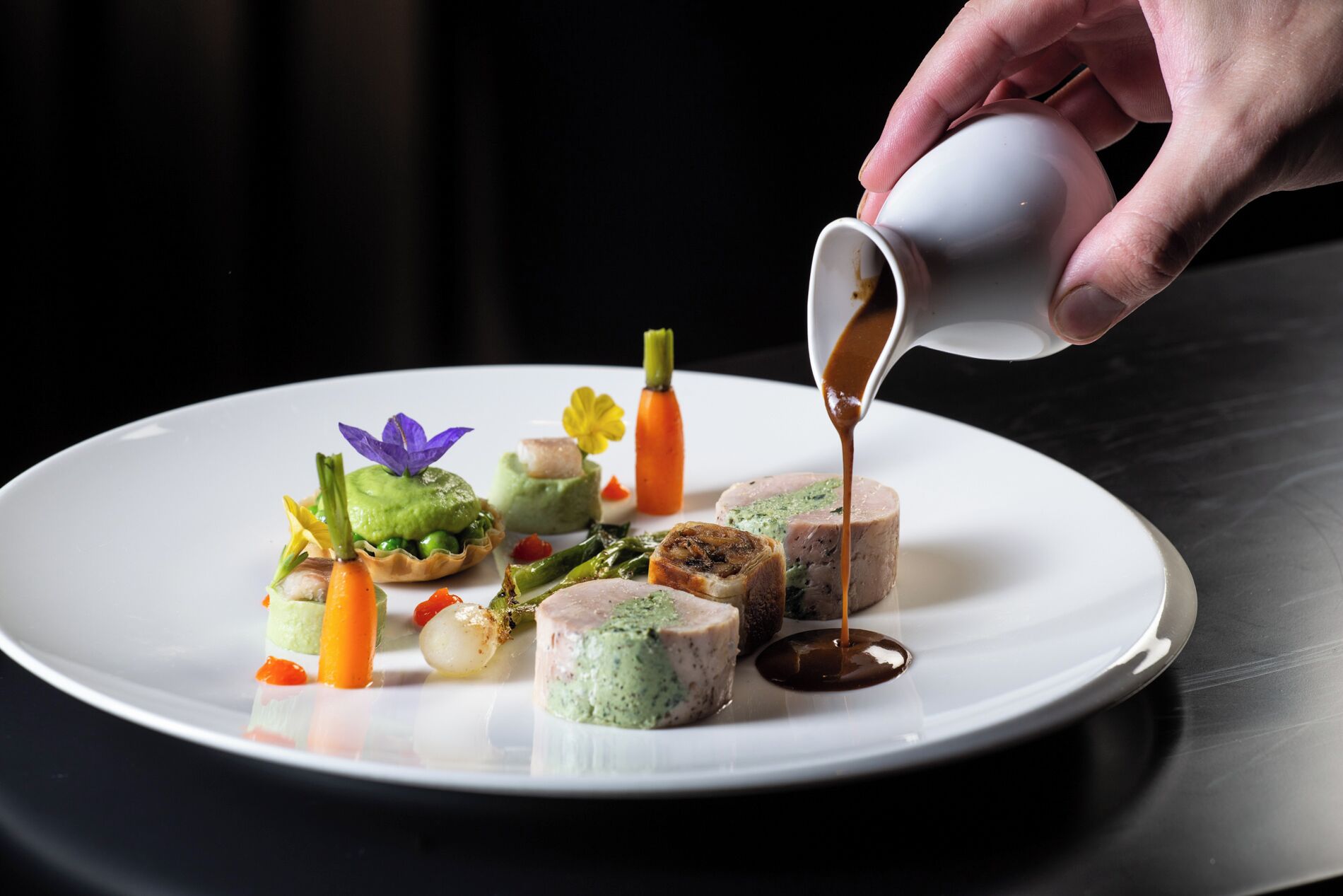 Une assiette blanche contenant divers aliments, notamment une tarte verte, une tranche de viande avec une garniture verte et un petit morceau de carotte.