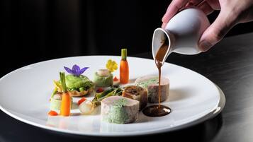 A white plate with various food items, including a green tart, a slice of meat with green filling, and a small piece of carrot.