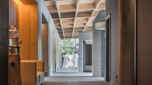 Un couloir moderne avec un banc en bois, une grande colonne cylindrique et, au loin, une vue sur un espace de détente.