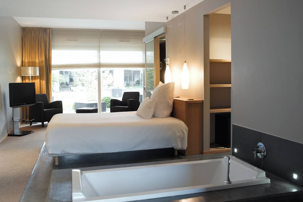 A modern hotel room with a large bed, a TV, a desk, and a bathtub.