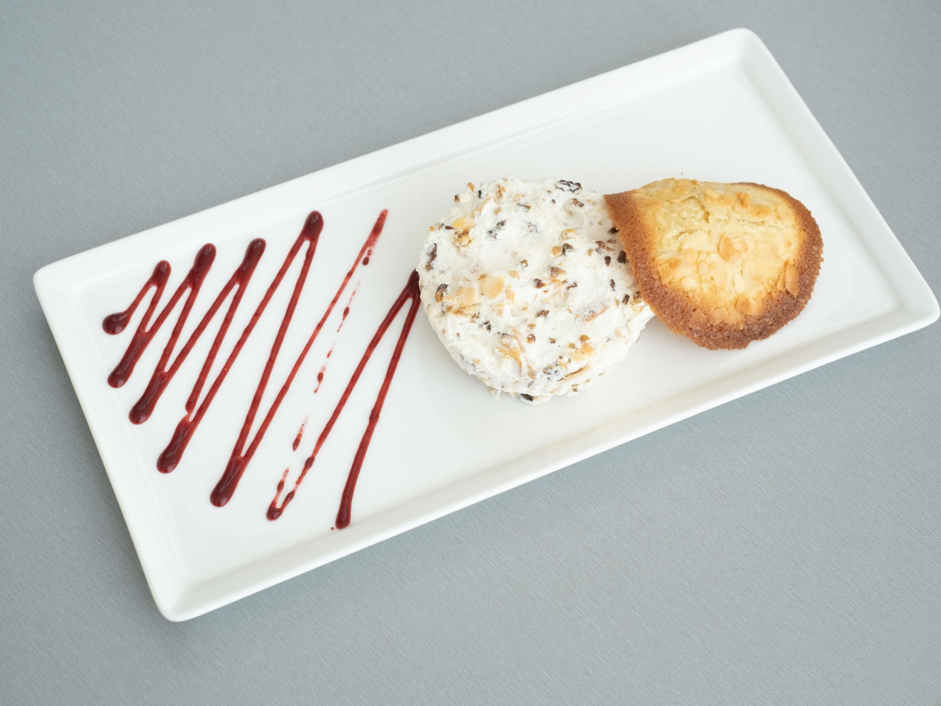 A dessert on a white rectangular plate with chocolate drizzle.
