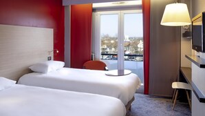 Une chambre d’hôtel avec deux lits, un bureau, une chaise, une télévision et une fenêtre donnant sur la ville.