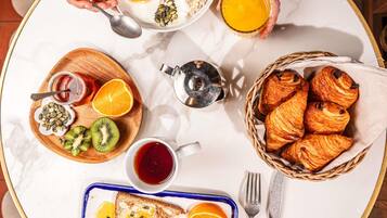 A breakfast setting with croissants, orange slices, and a cup of tea on a round table.