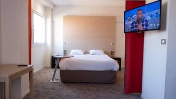 Una habitación de hotel con cama, televisor montado en la pared, escritorio y ventana.